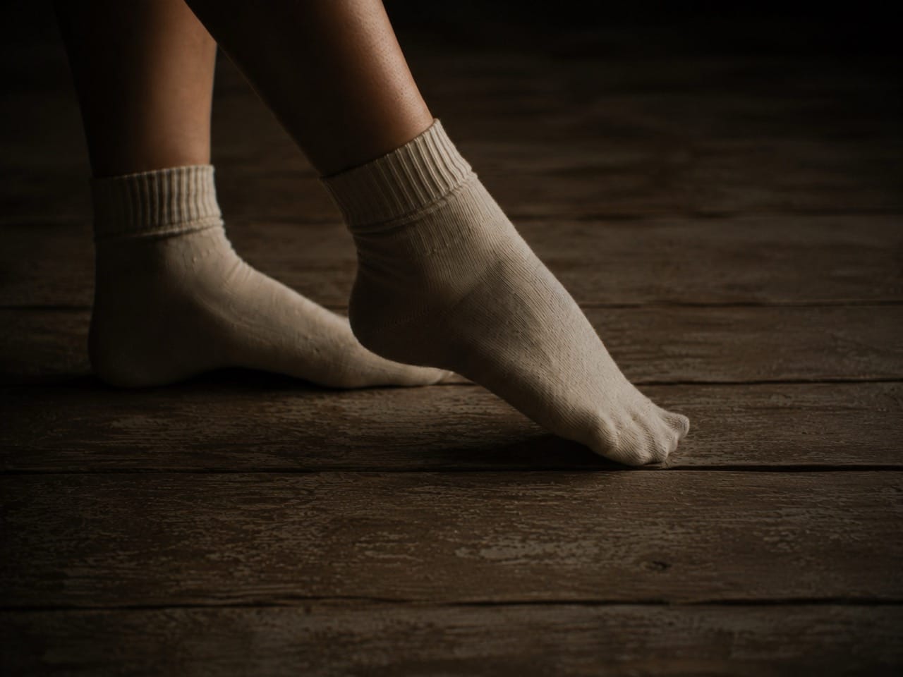 A woman wearing socks feels the cracks in old, worn floorboards with her feet